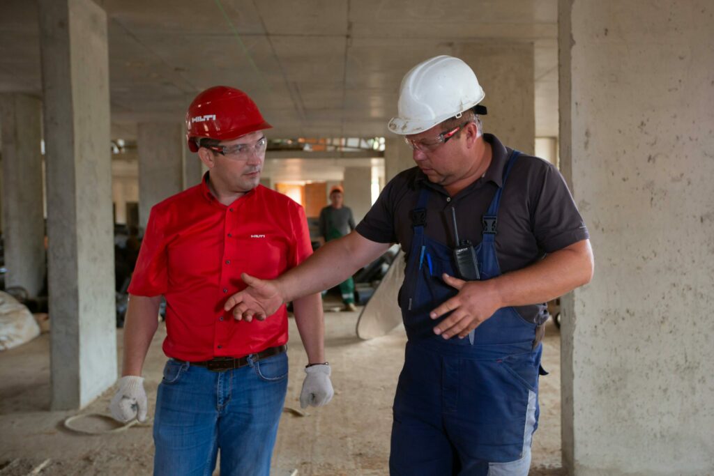 Two construction workers in safety gear discussing plans at a construction site.